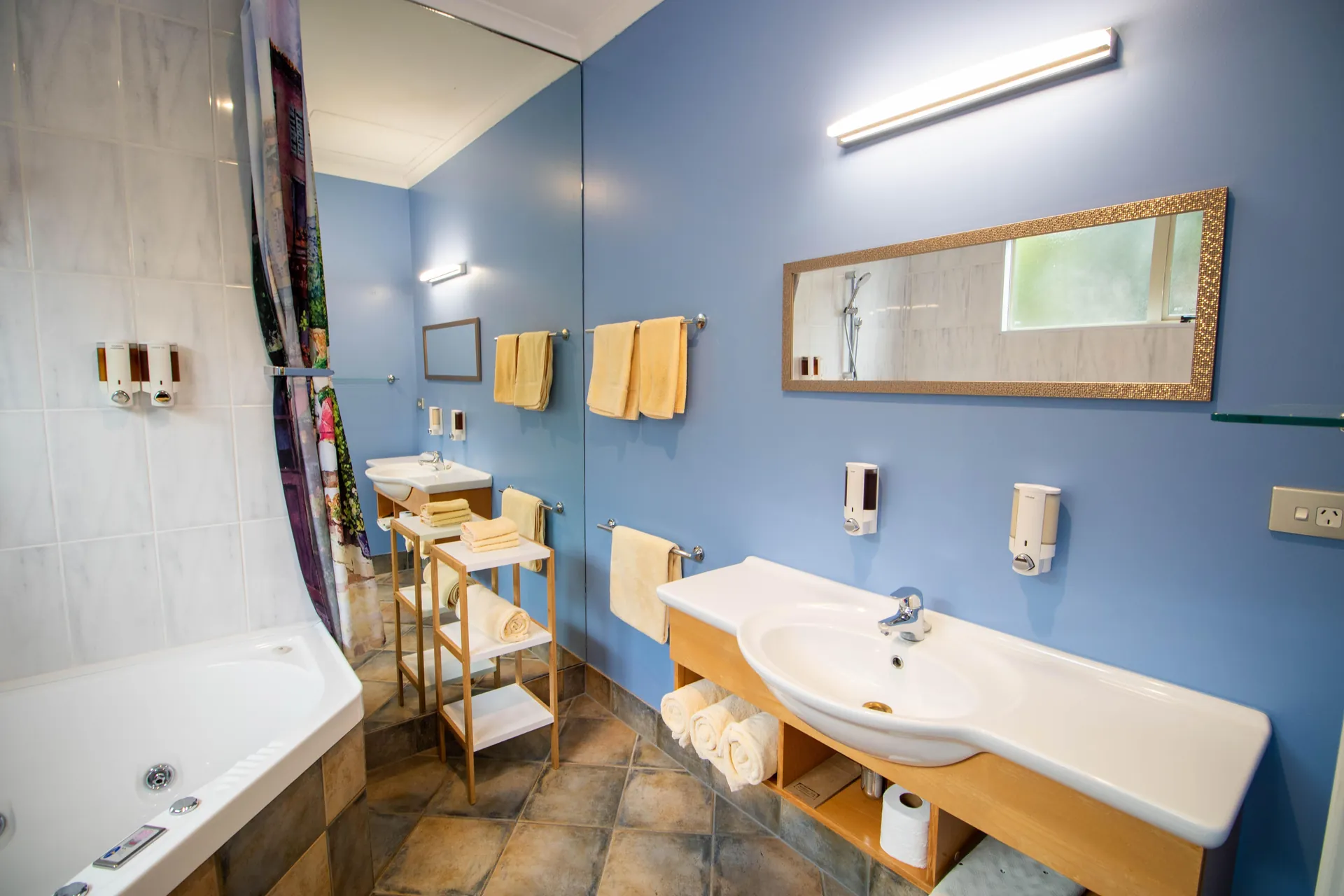 One Bedroom Unit Bathroom One bedroom unit bathroom with spa bath, vanity and towels against a blue feature wall