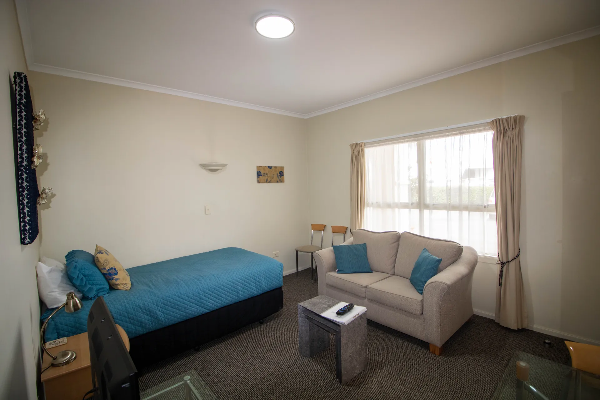 One Bedroom Unit Lounge Single Bed Living room with single bed and two seater sofa beside a bright window in the one bedroom unit