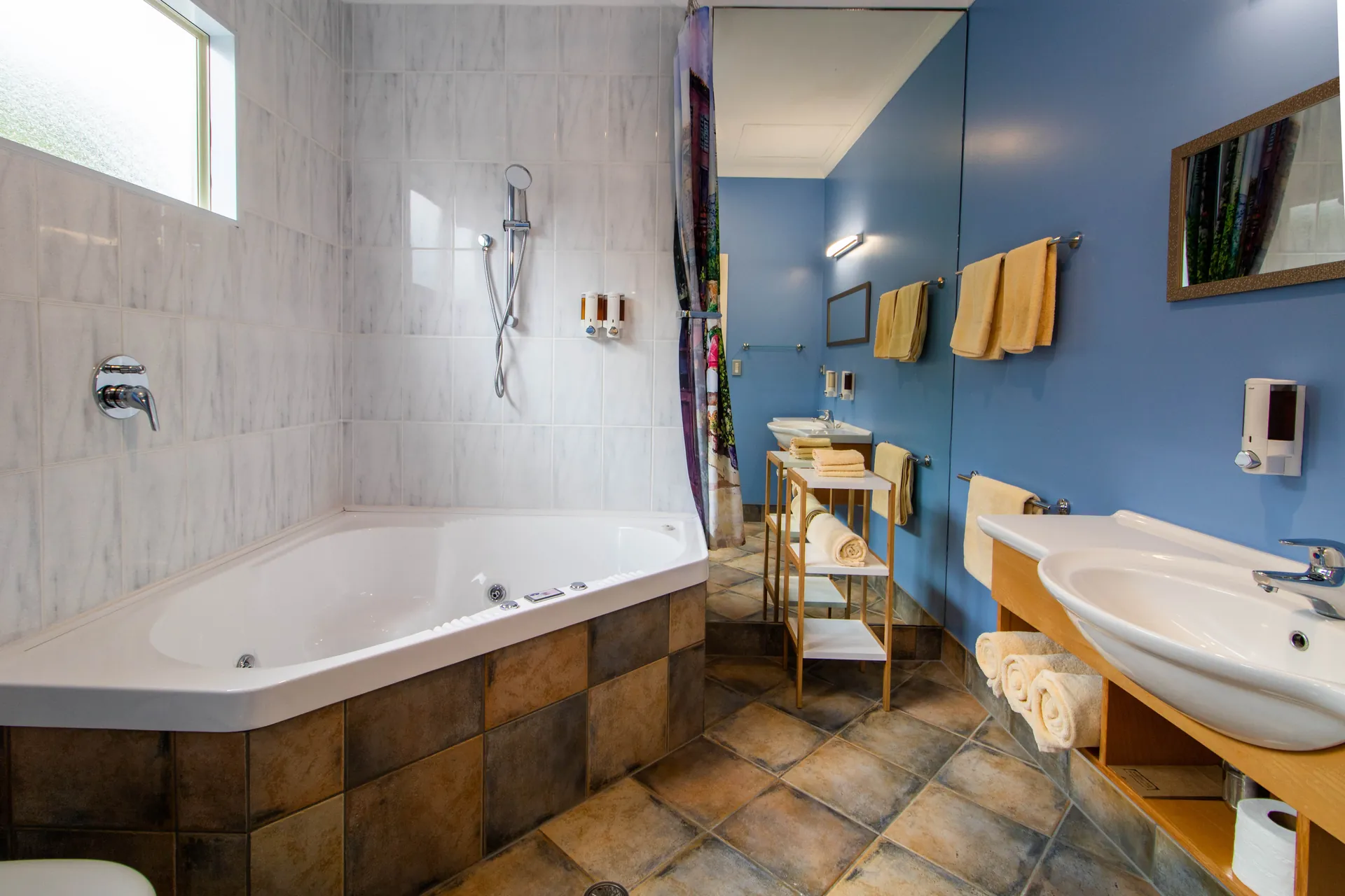 One Bedroom Unit Spa Bath Corner spa bath with overhead shower and terracotta tiles in the one bedroom unit bathroom
