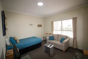 One Bedroom Unit Lounge Single Bed Living room with single bed and two seater sofa beside a bright window in the one bedroom unit