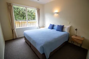 Two Bedroom Unit Main Bedroom Main bedroom with queen bed in blue linen beside a large curtained window in the two bedroom unit