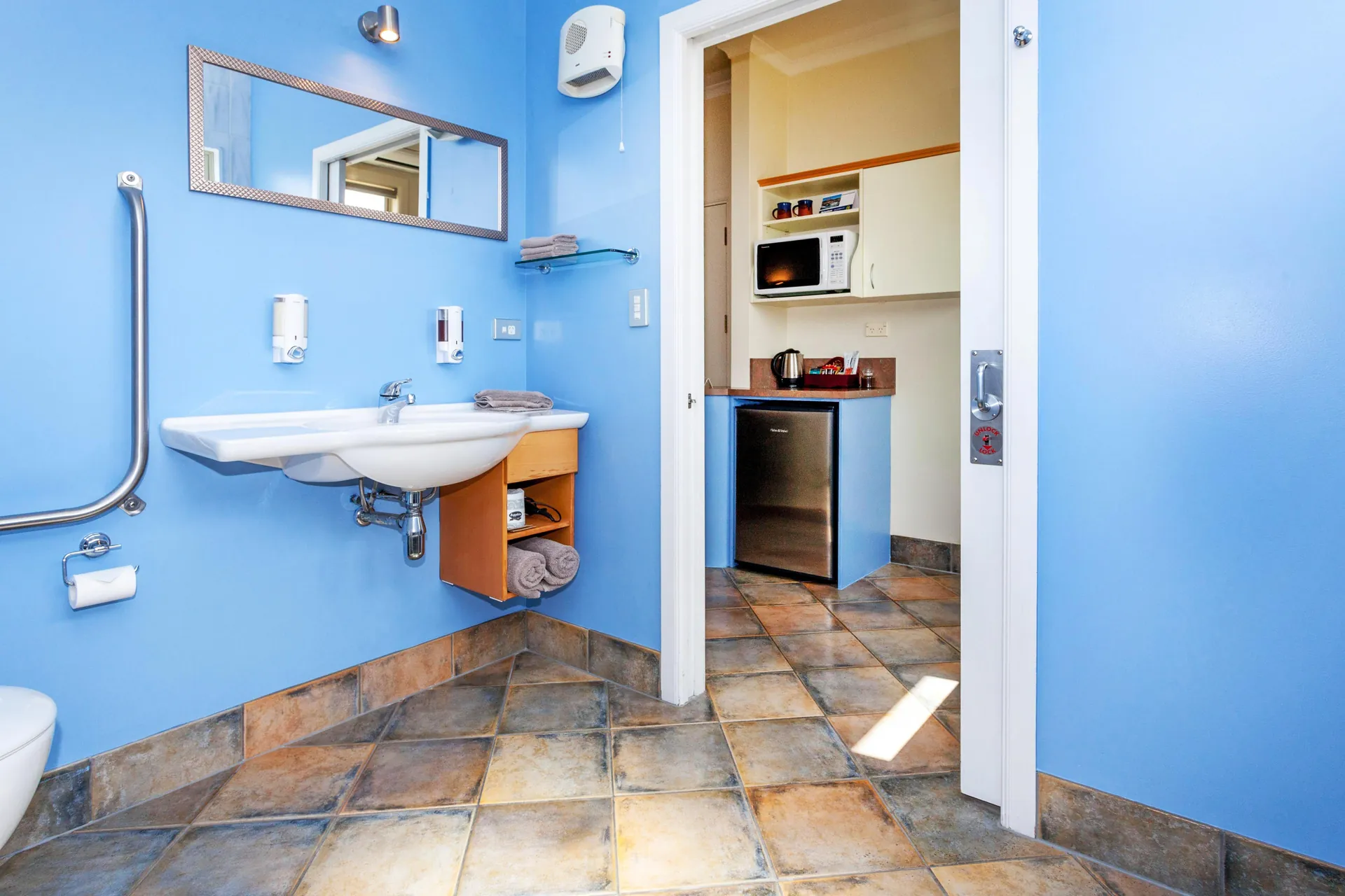 Access Studio Basin and Grab Rails Accessible height basin with grab rails and mirror, with the kitchenette visible through the doorway