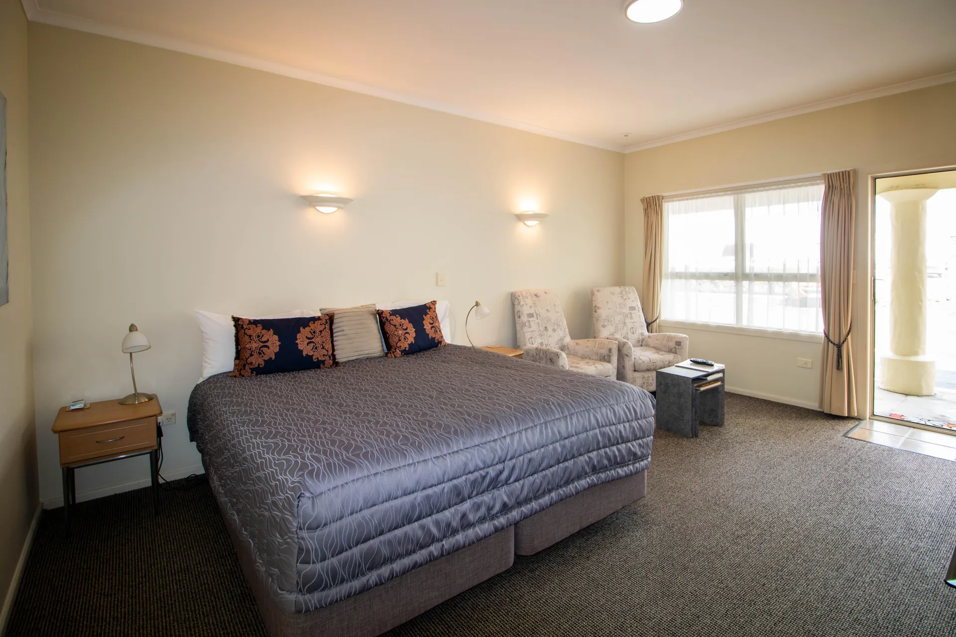 King Studio King Bed King bed with decorative cushions beside armchairs and a bright curtained window in the King Studio