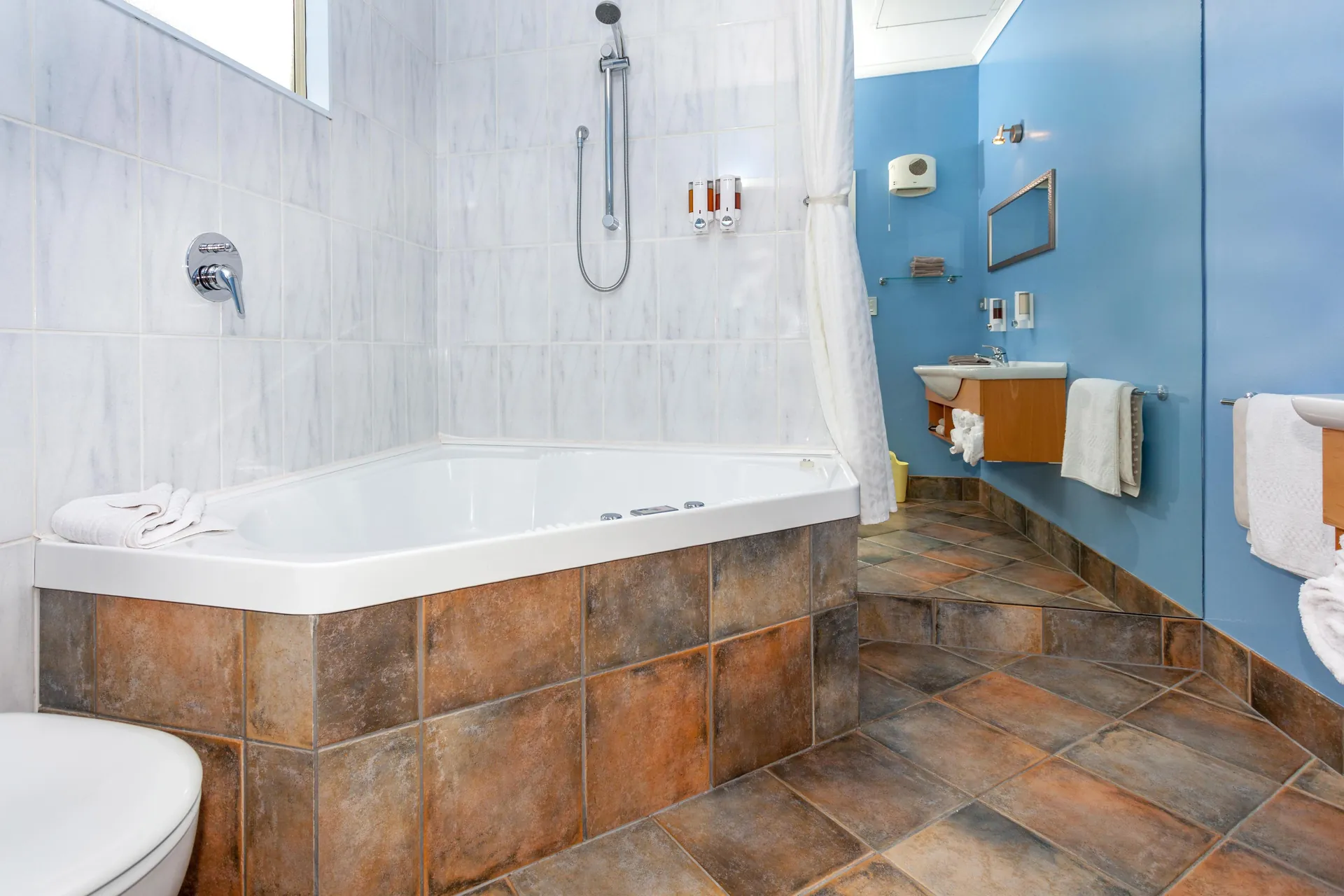 King Studio Spa Bath Corner spa bath with overhead shower, terracotta tiles and blue walls in the King Studio bathroom